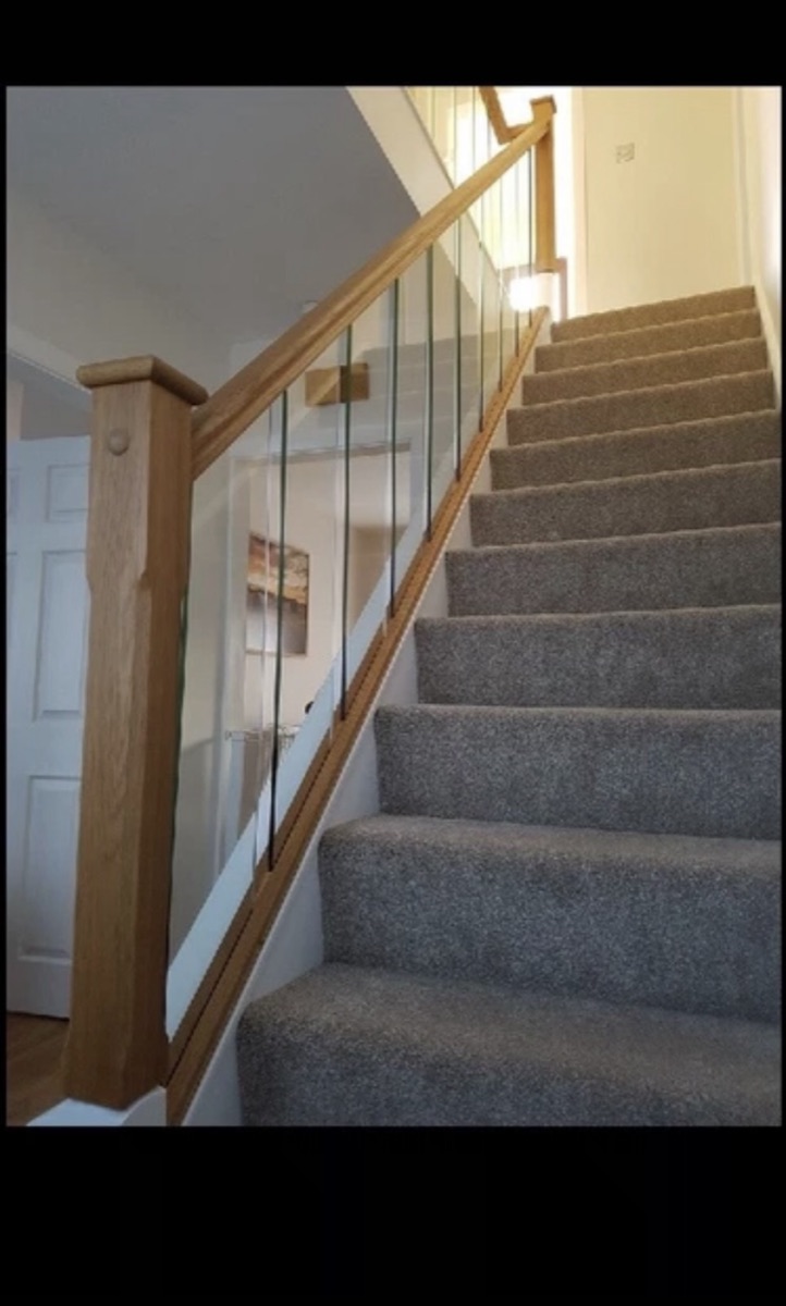Oak newel and frameless glass balustrade to a carpeted staircase