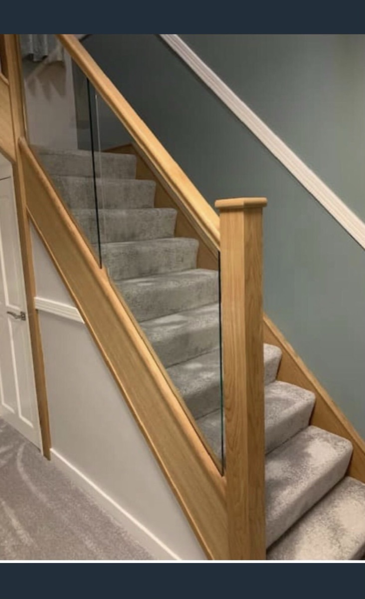 Solid oak staircase with a full-height glass side panel against a green feature wall